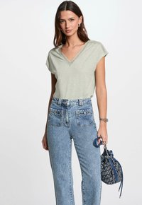 Lichtgroene V-hals shirt met kantdetails bij de halslijn, gecombineerd met hoge lichtblauwe denim jeans en een handtas met patroon.
