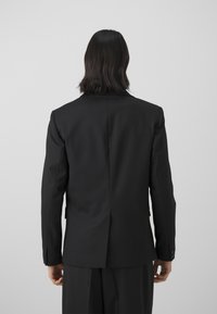 Black tailored blazer with a notch lapel, structured shoulders, and a single vent at the back. Smooth fabric and three-button cuffs.