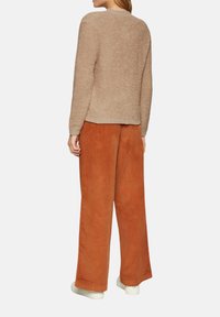 Beige strukturierter Pullover mit langen Ärmeln, Rundhalsausschnitt und geripptem Saum, kombiniert mit weit geschnittenen Cordhosen in Rostfarbe.