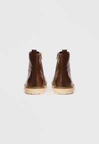 Braune Leder-Ankelstiefel mit glatter Oberfläche, seitlichen elastischen Einsätzen und einer beigen Gummisohle. Mit Zugschlaufen an der Rückseite.