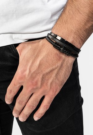 Black leather and braided bracelets in varying widths on a wrist, featuring smooth and textured surfaces, without additional embellishments.