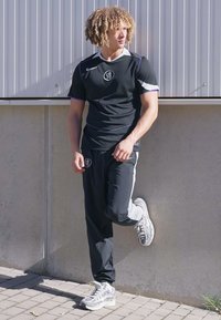 Black athletic t-shirt with white and purple accents, paired with black track pants featuring side stripes and grey running shoes.