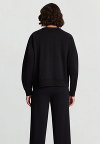 Schwarzer Baumwollpullover mit Raglanärmeln, gerippten Bündchen und Saum. Die Rückansicht zeigt eine entspannte Passform und eine glatte Textur.