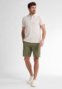 Beige short-sleeve polo shirt with a collar and three-button placket, paired with olive green shorts and white sneakers.