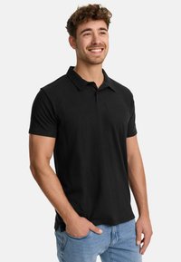 Polo negro de algodón, con cuello y mangas cortas. El diseño incluye un logo sutil en el pecho. Corte clásico.