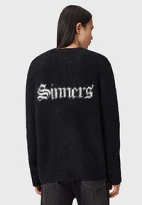 Zwarte fluffy sweater met een ronde hals. "Sinners" in gedetailleerd witte lettertype op de achterkant. Zachte textuur, relaxte pasvorm, schoudernaden vallen iets af.