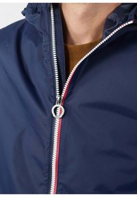 Giacca con zip blu navy con collo alto, caratterizzata da una zip bicolore: bianca e rossa. Tessuto liscio con una sottile lucentezza. Accessori in argento.