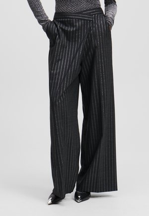 Black pinstriped wide-leg trousers with a wrap design, featuring a smooth texture and side pockets, paired with metallic pointed shoes.