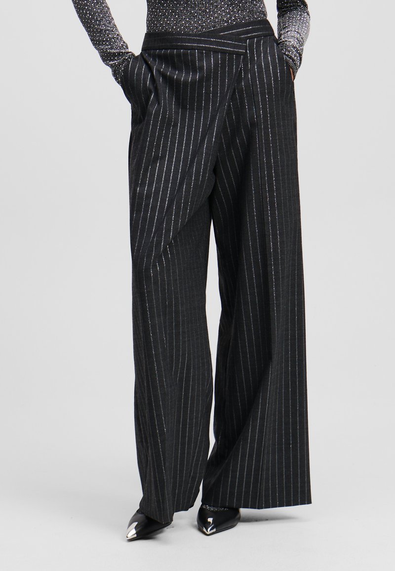 Zwarte gestreepte brede pijpen broek met een wikkeldesign, voorzien van een gladde textuur en zijzakken, gecombineerd met metalen puntige schoenen.