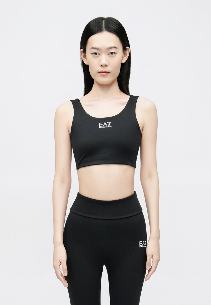 Fekete, rugalmas anyagból készült crop top kerek nyakkivágással és logó részlettel. Hozzáillő magas derekú leggingsszel párosítva.