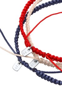 Tre flätade armband gjorda av röda, marinblå och krämfärgade snören, med små silverfärgade metalltaggar med ingraverade siffror.