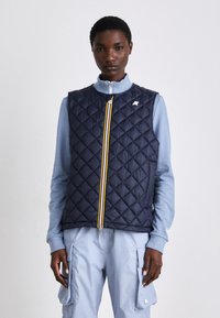 Navy quilted vest with a high collar, featuring a multicolored zipper and a small logo on the chest, worn over a light blue top.