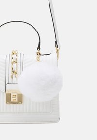Hvid quiltet håndtaske med gulddetaljer, en kædeaccent, sort kant og en aftagelig, fluffy hvid pompon. Justerbar skulderrem medfølger.