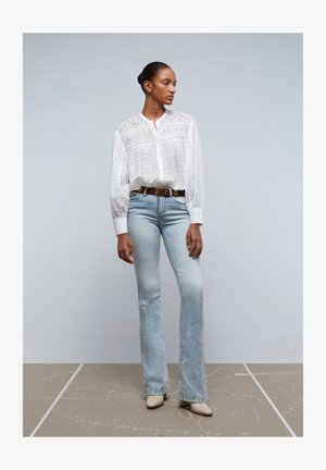 Witte eyelet blouse met knopenfront, hoge kraag en lange mouwen; lichtblauwe uitlopende jeans met een versleten detail; beige hoge muiltjes.