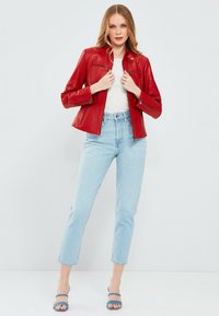 Rode leren jas met een getailleerd ontwerp, ritszakken en een ingekorte silhoutte, gecombineerd met lichtblauwe high-waisted jeans.