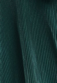 Tissu vert foncé avec des plis verticaux, texture lisse avec un léger brillant, mettant en valeur un design sophistiqué et structuré.
