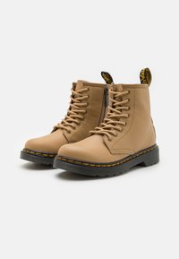 Botas de tobillo de cuero marrón con suelas de goma negras, costuras amarillas en contraste, cordones en la parte delantera y una cremallera lateral.