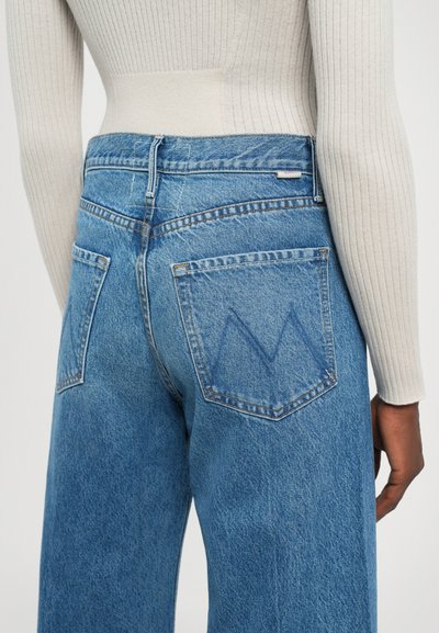 Light blue denim jeans with a relaxed fit, featuring two back pockets and a subtle "M" stitching detail. Tapered leg with a medium rise.