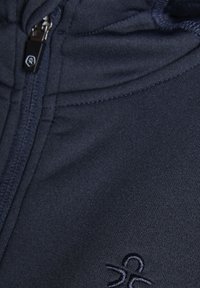 Marinblå hettegenser med glidelås, laget av mykt materiale, med en teksturert overflate og brodert logo detaljer på forsiden nær glidelåsen.