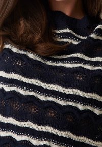 Navy- und weiß gestreifter Pullover mit wellenförmigem Muster und offenen Strickdetails. Rippkragen und Texturvariationen im gesamten Design.