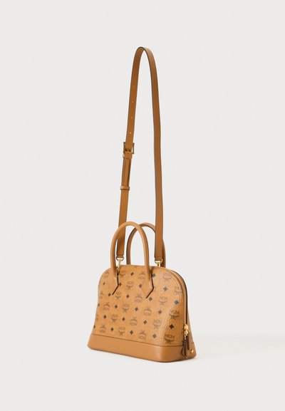Sac à main en cuir camel avec deux anses courtes, une longue bandoulière réglable et un motif de logo MCM répété sur fond blanc uni.