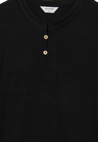 Maglietta henley nera realizzata in tessuto testurizzato, con una piccola patta e due bottoni in legno e un colletto arrotondato. Etichetta della taglia: L.