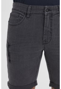 Shorts in denim nero con dettaglio consumato sulla gamba sinistra, orlo arrotolato e design tradizionale con cinque tasche.