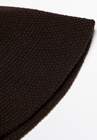 Close-up of folded dark brown knitted fabric with textured, waffle-like pattern on white background.