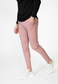 Pantalons ajustés rose clair en tissu mélangé de coton, avec des poches latérales et associés à des baskets blanches chunky sur un fond neutre.