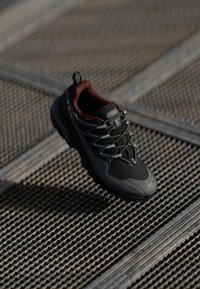 Black and gray outdoor shoe with a mesh upper, red accents, reflective laces, and a thick sole, designed for durability and traction.