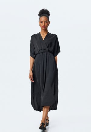 Sorte midi-kjole med omslag, korte ærmer, en indsnævret talje og en blød tekstur. Kombinationen med sorte vævede sandaler.