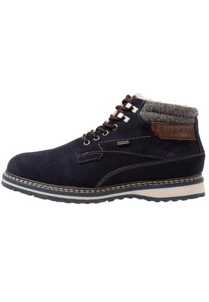 Bottine en daim bleu marine avec lacets marron, col en laine, semelle en caoutchouc, surpiqûres blanches et écusson logo Bugatti en cuir marron.