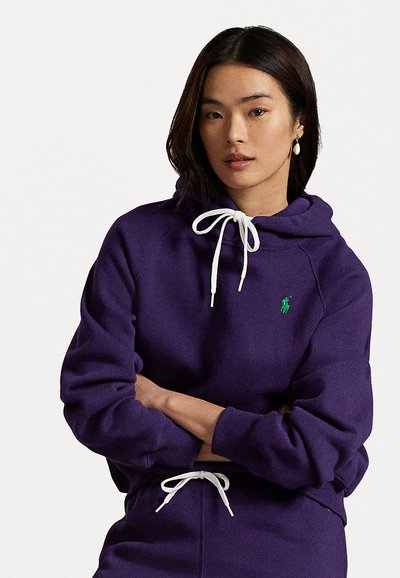 Purple hoodie with a drawstring, white accents, and a small green emblem. Textured fabric with a relaxed fit and ribbed cuffs.