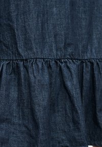 Σκούρο μπλε τζιν ύφασμα με ραμμένο, ρυτιδωμένο σχέδιο ραφής που δημιουργεί μια υφή σε στρώσεις.