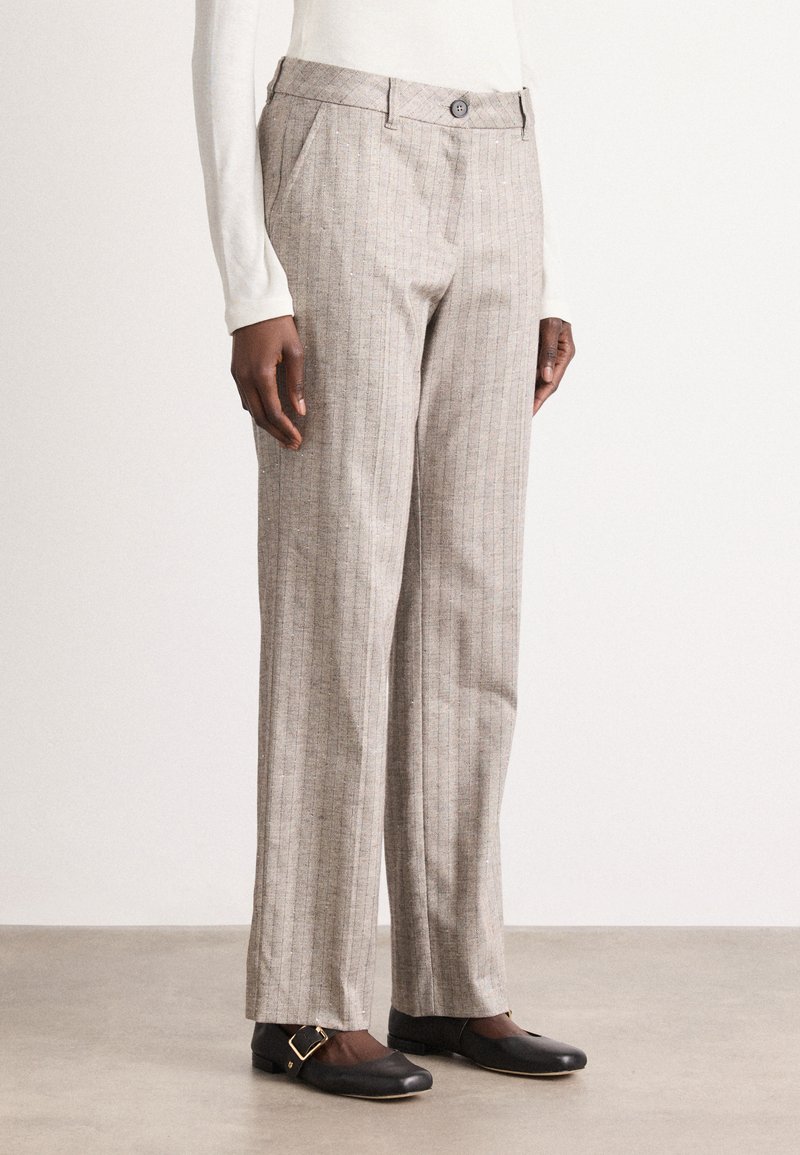 Person wearing beige pinstripe straight-leg trousers paired with black flat shoes with gold buckle details.
