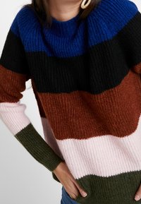 Kolorowy dzianinowy sweter z poziomymi paskami w kolorach niebieskim, czarnym, brązowym, różowym i zielonym. Żebrowana struktura z luźnym krojem.