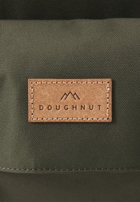 Green fabric bag with a textured surface and a brown leather patch embossed with "DOUGHNUT" and mountain logo. Stitched edges are visible.