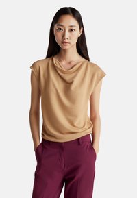 Krémový bezrukávový top s volným výstřihem a jemnou texturou, spárovaný s burgundskými kalhotami. Top má uvolněný střih a hladkou tkaninu.