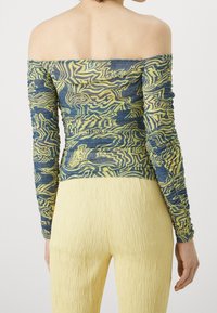 Off-the-shoulder top in blue and yellow abstract pattern, fitted design with long ruched sleeves; paired with textured yellow pants.