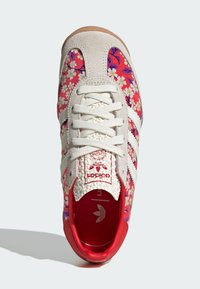 Röda sneakers med blommönster, i kombination med ljusbeige mockaskinn, vita ränder och röd inredning. Utrustad med texturerade snören och gummisula.