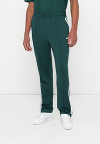 Grønne treningbukser med en avslappet passform, med hvite sidestriper og elastisk midjebånd, kombinert med hvite joggesko.