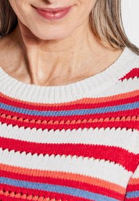 Gebreide trui met horizontale strepen in rood, wit, blauw en koraal. Ribbelneklijn met open brei details tussen de strepen.