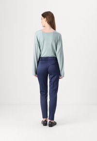 Světle modrý top s dlouhým rukávem v kombinaci s námořnickými kalhotami na míru. Oblečení doplňují černé slip-on boty. Minimalistický design a střih.