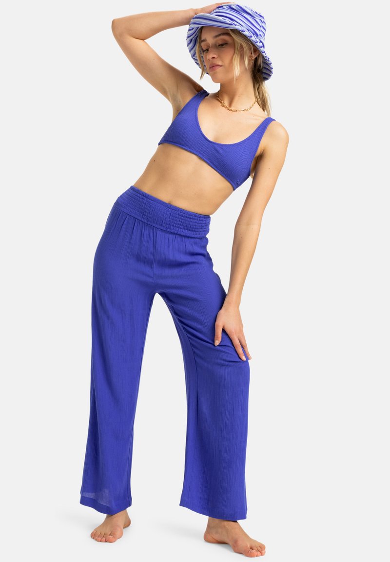 Top corto azul acanalado y pantalones de pierna ancha con cintura elástica. Un sombrero tipo cubo a rayas azul y blanco a juego completa el conjunto.