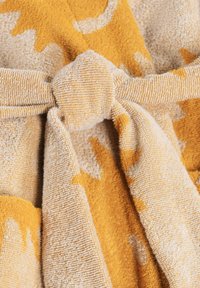 Primo piano di un fiocco in tessuto testurizzato beige e giallo senape con un motivo astratto, che mostra anelli e pieghe del materiale.