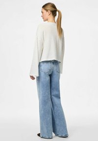 Maglione corto a righe bianche con maniche ampie abbinato a jeans a vita alta, di un blu chiaro e a gamba larga. Tessuto morbido e vestibilità comoda.