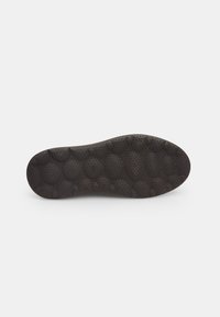 Black rubber shoe sole featuring a textured surface with raised circular patterns and a wavy shape, designed for comfort and traction.