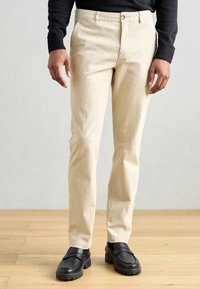 Beige cotton trousers with a straight leg design, featuring a button closure and side pockets, paired with black loafers.