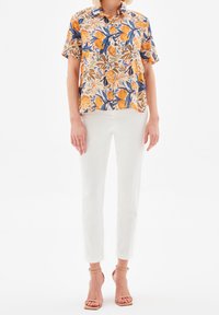 Short-sleeve button-up shirt featuring a vibrant orange and blue floral print, paired with slim white trousers and nude heeled sandals.
