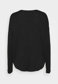 Chemise noire à manches longues avec une coupe décontractée, un ourlet arrondi et un tissu doux et texturé avec des coutures minimales, conçue pour le confort.